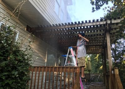 A man on a ladder painting the roof of a house.
