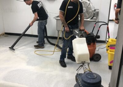 Two men are cleaning a floor with machines.