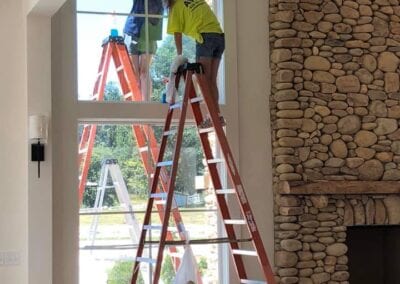 Two men are working on a ladder in front of a window.