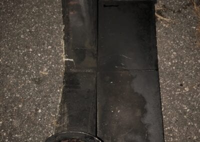 A black pipe sitting on the ground next to a metal object.
