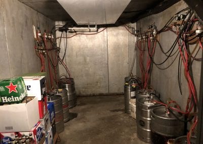 A room with many beer kegs and wires hanging from the ceiling.
