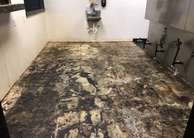 A dirty floor with a sink and toilet in the background.