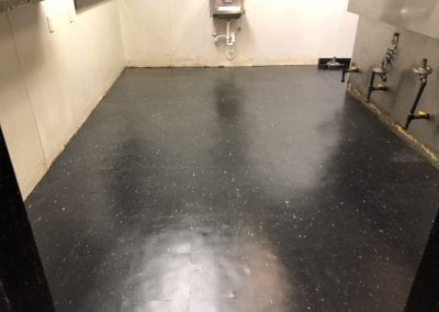 A black floor with white walls and a metal sink.