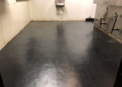 A black floor with a sink and mirror in the corner.
