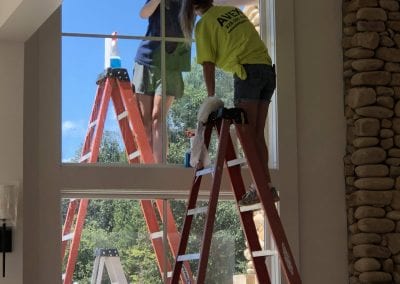 Two people on ladders working on a window.