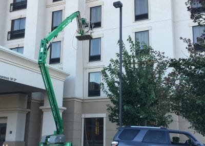 A green crane is in the air next to a building.